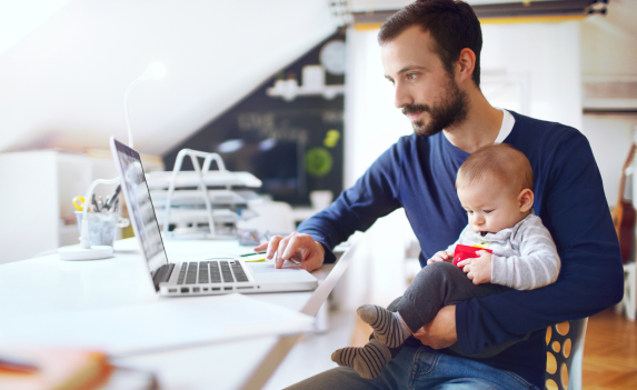 Father holding his baby and working on computer